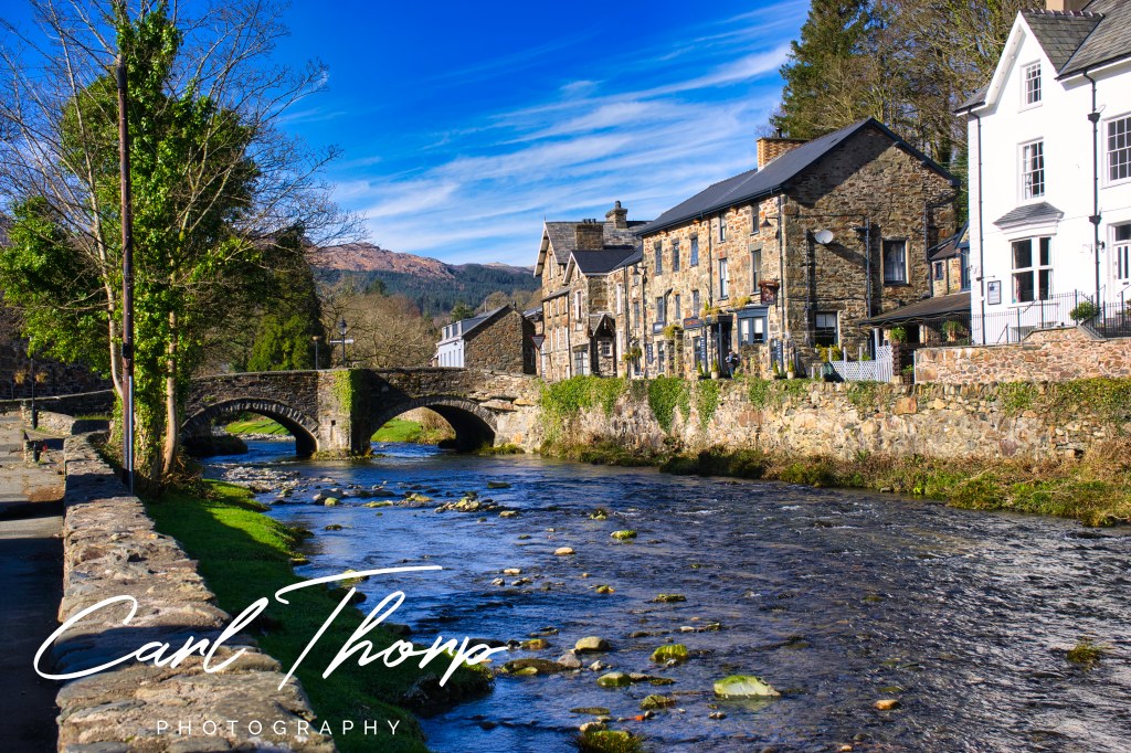 View up the river towards the road bridge in Beddgelert on a sunny day.